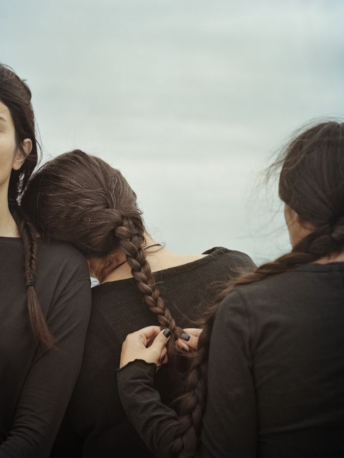 trois femmes dont l’une tresse les cheveux de l’autre