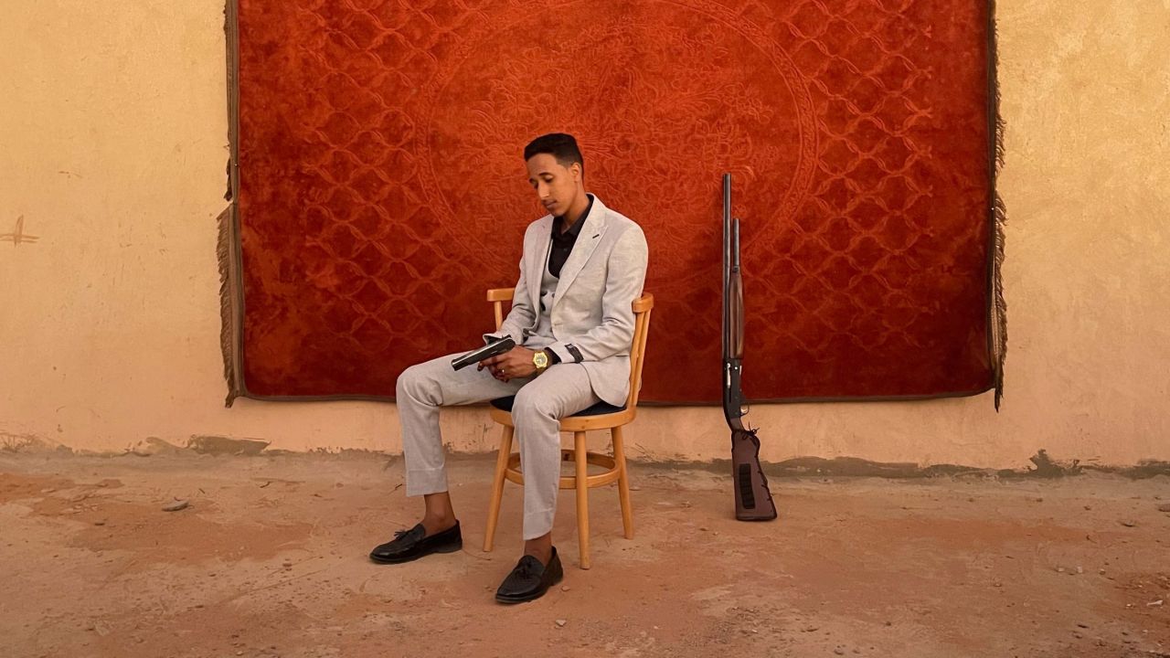 homme tenant un revolver devant un tapis rouge